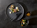 Gourmet dish with black plate and cutlery on a dark surface